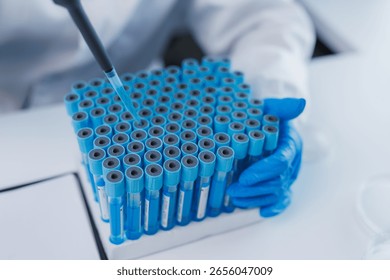 Gloved scientist adding blue liquid to test tubes using a pipette in laboratory, conducting scientific research or medical tests