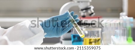 Gloved scientist holds test tube with transparent liquid and types on keyboard. Chemical research results concept