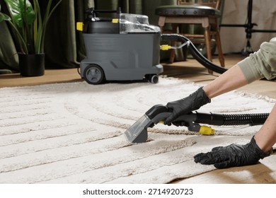 Gloved worker uses extraction machine to deep clean beige rug in cozy living room interior