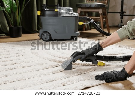 Gloved worker uses extraction machine to deep clean beige rug in cozy living room interior