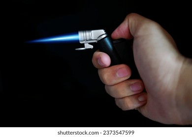 The glow of a gas lighter torch with hand in the dark. Close-up.