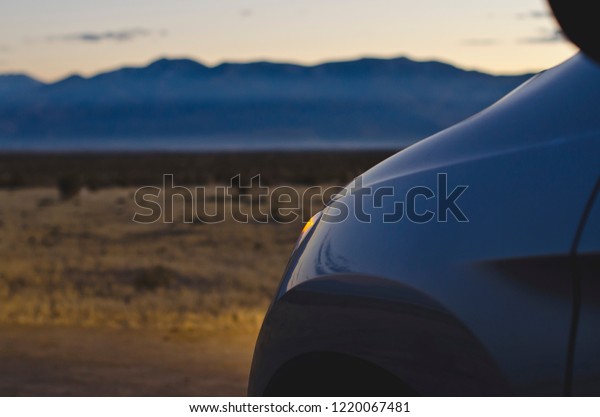 The glow of the lights from the\
setting sun and the car in the cool calm desert landscape\
