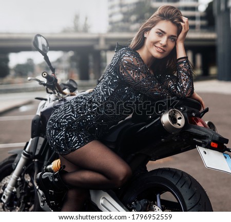 Glow streets and custom dark motorcycle with his beaty female owner. Cute girl's motosport hobby portrait. Urban motosport.