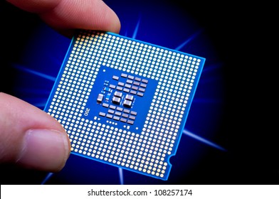 Glowing blue computer CPU held between finger and thumb in front of starburst on a black backgound