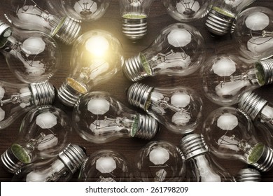 glowing bulb uniqueness concept. many bulbs on brown wooden table