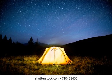 Glowing Camping Tent In The Night Mountain Forest Under A Starry Sky