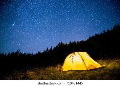 Glowing Camping Tent In The Night Mountain Forest Under A Starry Sky