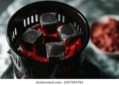 glowing coals heating in an electric charcoal lighter for shisha, with a blurred tobacco bowl in the background in a traditional Arabic hookah lounge.  - Powered by Shutterstock - Get 15% off with code: PIKWIZARD15