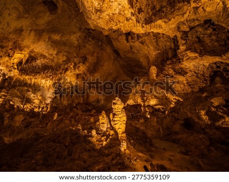 Glowing formations hang from the cavern ceiling while towering columns rise from the rocky floor.