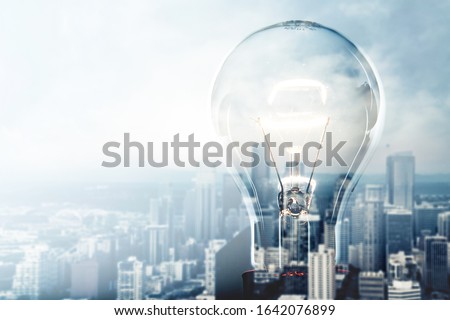 Glowing glass light bulb on city background