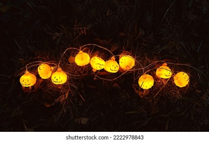 Glowing jack-o' lanterns garland on dark grass, abstract blurred natural background. symbol of Halloween holiday, Samhain sabbat. festive autumn season. top view - Shutterstock ID 2222978843