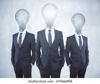 Glowing Lamp Headed Businessmen On Concrete Background. Inovation Concept 