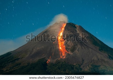 glowing lava flow of mount merapi eruption at night with star trail background