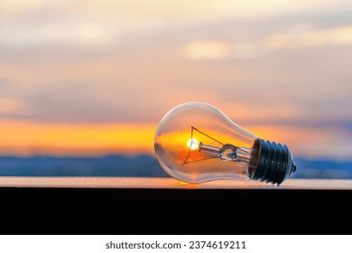 Glowing light bulb set against the backdrop of a setting sun. Clean energy and sustainability related concept. - Powered by Shutterstock