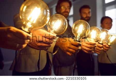 Glowing light bulbs in hands of creative business team in office as symbols of their ideas. Close up of turned on Edison bulbs in hands of men and women standing in row. Selected focus.