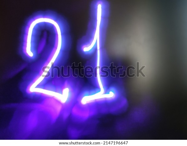 Glowing light purple\
number. On a dark glass matte background, the image of the number\
21 is made by hand. The light of a laser pointer was used to create\
the inscription.