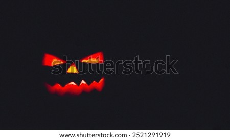 A glowing, menacing jack-o'-lantern face carved into a pumpkin, illuminated in the dark, creating a spooky Halloween atmosphere.