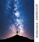 Glowing Milky Way and man on mountain peak at starry night. Silhouette of a guy on the hill, sky with bright stars. Galaxy. Space landscape with milky way. Nightscape. Travel background. Concept