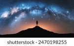 Glowing Milky Way and man on mountain peak at starry night. Silhouette of a guy on the hill, sky with bright stars. Galaxy. Space landscape with milky way arch. Panoramic nightscape. Travel. Concept