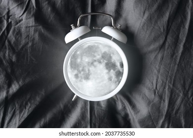 A glowing moon inside the alarm clock on the bed. Sleep time. Night rest. Waking up at night, insomnia. A nightmare. Creative alarm clock.