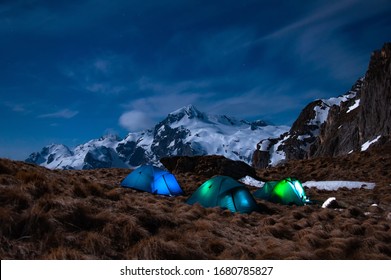 Glowing in the night tents on a background of snowy mountains.
