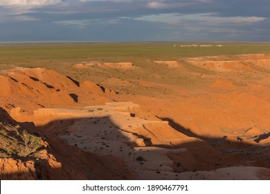 Glowing red rocks of the famous Mongolian Flaming Cliffs at sunrise with a scenic view across an isolated ger camp in the Gobi Desert all the way to the horizon