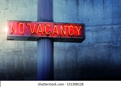 Glowing retro neon 'no vacancy' sign against cool blue wall background