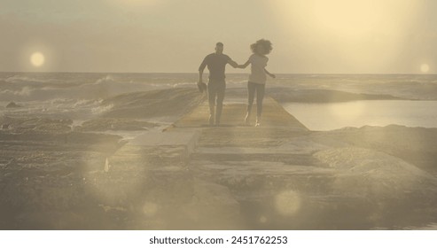 Glowing spots of light against african american couple holding hands running on the rocks. Love and relationship concept - Powered by Shutterstock