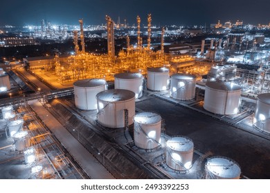 Glowing storage tanks and a labyrinth of pipes define an oil refinery under the cover of darkness, a testament to continuous industrial activity. - Powered by Shutterstock