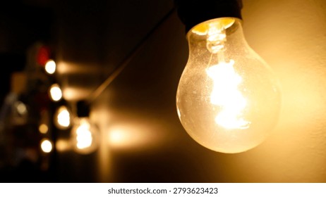 Glowing string lightbulbs creating warm amber illumination against a dark wall, presenting a cozy atmosphere with shallow depth of field highlighting the foreground bulb filament