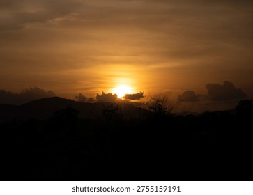 Glowing Sun Setting Over Distant Mountain Range and Silhouetted Forest