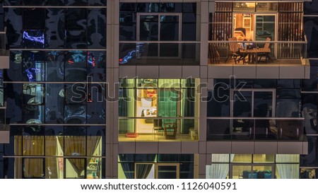Glowing windows of skyscrapers at evening timelapse. View of modern residential high-rise buildings in Dubai marina. People moving inside apartments. Aerial top view. Pan down