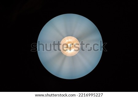 Glowing yellow incandescent light bulb on the background of the grey lampshade circle and black background. Light bulb in a round lampshade. Bottom view