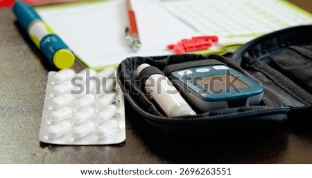 A glucometer set, notebook, and medication are organized on a table in the living room. The setup assists in daily blood sugar monitoring and diabetes management routines.