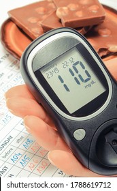 Glucometer With Sugar Level In Hand And Portion Of Chocolate On Medical Form With Results Sugar Level