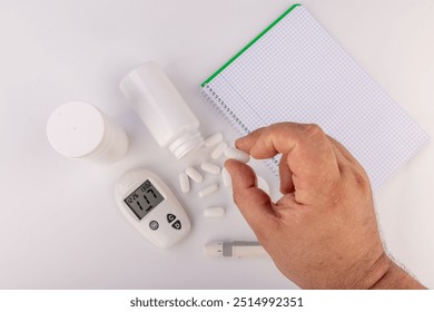 A glucose meter, note pad, white pills, and a hand taking a pill are arranged on a white background, showing a clear, organized setup for health management - Powered by Shutterstock