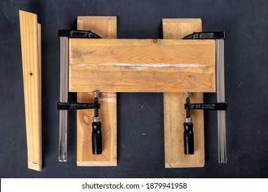 Gluing Pieces Of Wood With Carpentry Glue. Boards In Carpentry Clamps. Dark Background.