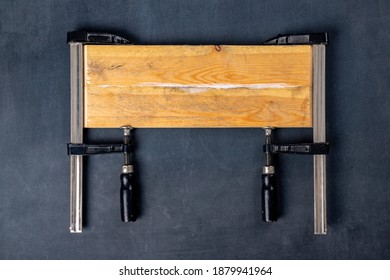 Gluing Pieces Of Wood With Carpentry Glue. Boards In Carpentry Clamps. Dark Background.