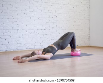 Gluteal bridge on pink small fitness ball. Young caucasian woman doing pilates with special equipment in fitness studio. Work out, yoga, balance, concentration, equilibrium, healthy spine, sport