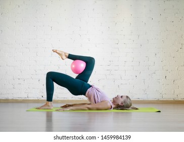Gluteal bridge with pink small fit ball. Caucasian girl doing pilates with special equipment in fitness studio. Work out, yoga, balance, concentration, healthy spine, sport, smart body and wellness