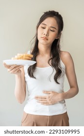 Gluten allergy, asian young woman hand holding, refusing to eat, looking at bread slice on plate in breakfast food meal at home, having a stomach ache. Gluten intolerant and Gluten free diet concept. - Shutterstock ID 2293109995