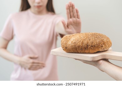 Gluten allergy, asian young woman hand push out, refusing to eat white bread loaf on board in breakfast food meal at home, girl having a stomach ache. Gluten intolerant and Gluten free diet concept.