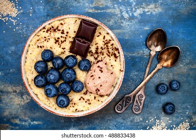 Gluten Free Amaranth And Quinoa Porridge Breakfast Bowl With Blueberries And Chocolate Over Vintage Blue Background. Top View, Overhead, Flat Lay. Copy Space