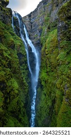Glymur waterfall flows dramatically through a verdant canyon in Iceland, showcasing the natural beauty of the landscape. The vibrant moss covers the rocky walls, creating a serene atmosphere.
