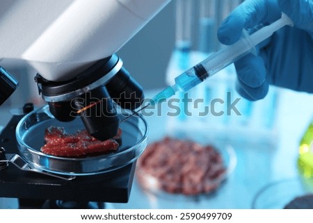 GMO concept. Scientist injecting something into piece of meat under microscope in laboratory, closeup