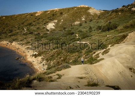 Gnajn Tuffieha, Malta - April 19, 2023: 
Landscape with a woman walking on the clay hills at Ghajn Tuffieha bay, Malta. 