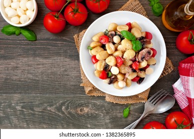 Gnocchi with tomatoes, mozzarella, mushrooms and basil. Above view corner border over a dark wood background with copy space. - Shutterstock ID 1382365895