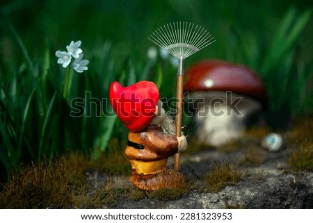 Gnome gardener with a rake.Mushroom meadow with bright flowers.Working gnomes in a fairy garden.Curious gnome in search of mushroom places.
