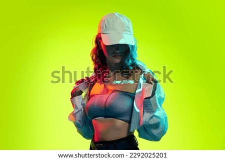 Go ahead. Portrait of young girl with hidden face under a cap and digital neon filter lights with inscryption on body on bright green background. Concept of digital art, fashion, cyberpunk, futurism