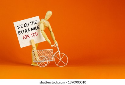 Go Extra Mile Symbol. White Sheet Of Paper. Words 'we Go The Extra Mile For You'. Miniature Bicycle And Wooden Model Of Human. Beautiful Orange Background. Business And Support Concept, Copy Space.